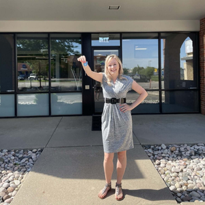 A woman holding up keys in front of a building.
