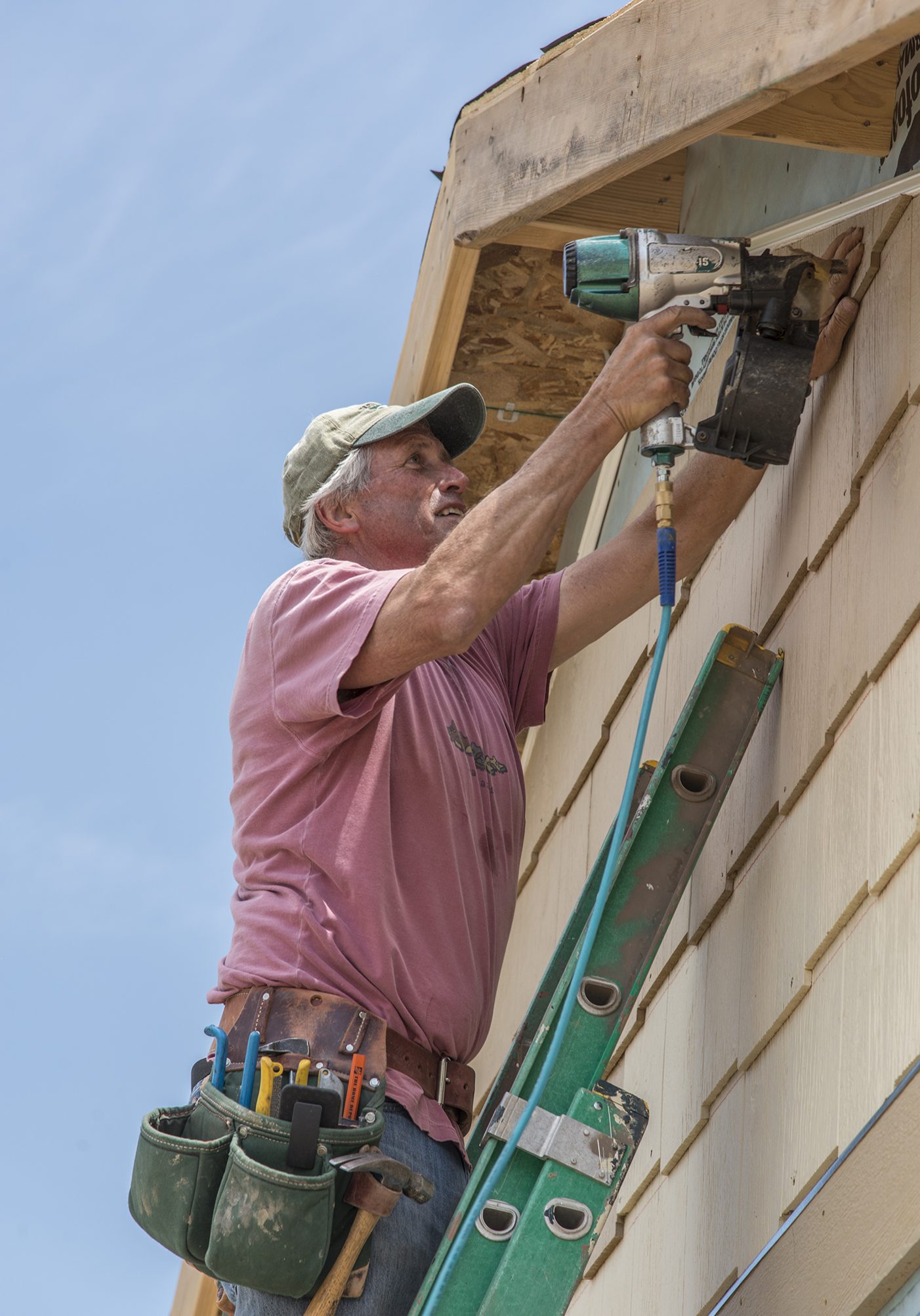 Loveland Habitat for Humanity Person on ladder with nail gun attaching siding to house.